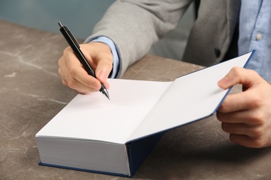 Photo of Writer signing autograph in book at table, closeup