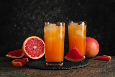 Photo of Tasty grapefruit drink with ice in glasses and fresh fruits on dark textured table