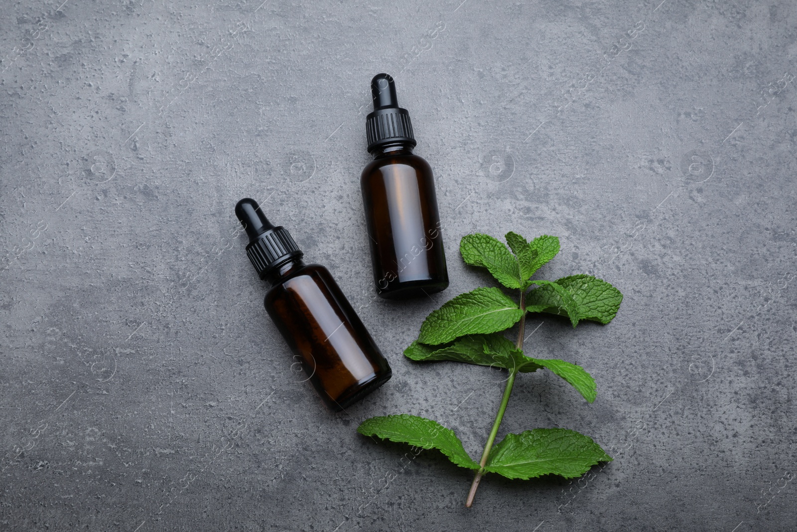 Photo of Bottles of essential oil and mint on grey table, flat lay