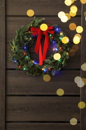 Beautiful Christmas wreath with red bow and festive lights hanging on door