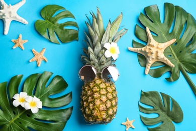 Photo of Flat lay composition with pineapple, sunglasses and beach items on light blue background. Creative concept