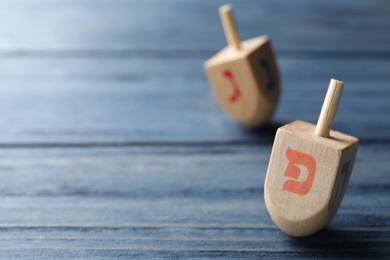 Hanukkah traditional dreidels with letter He on blue wooden table. Space for text