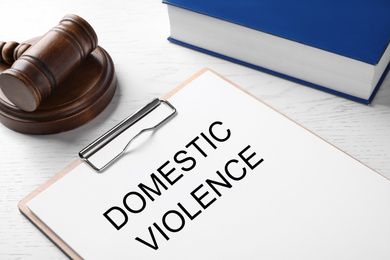 Photo of Clipboard with words DOMESTIC VIOLENCE and gavel on white wooden table, closeup
