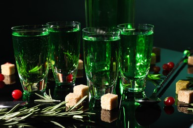 Photo of Absinthe in shot glasses, rosemary, brown sugar and spoon on mirror table. Alcoholic drink