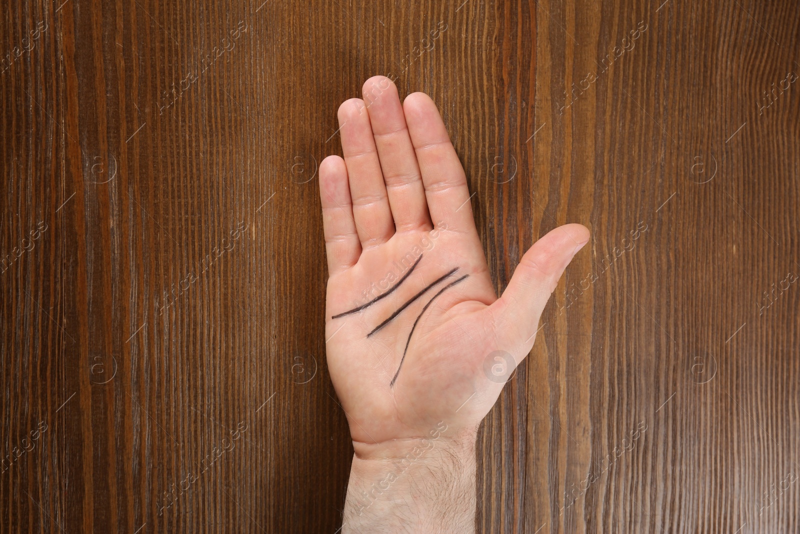 Photo of Man showing palm with drawn lines on wooden background, top view. Chiromancy and foretelling