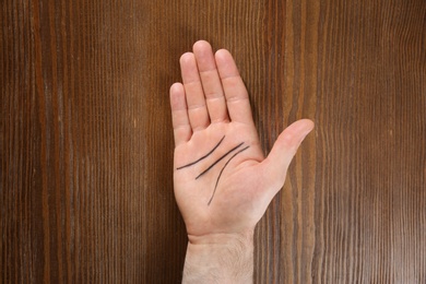 Photo of Man showing palm with drawn lines on wooden background, top view. Chiromancy and foretelling