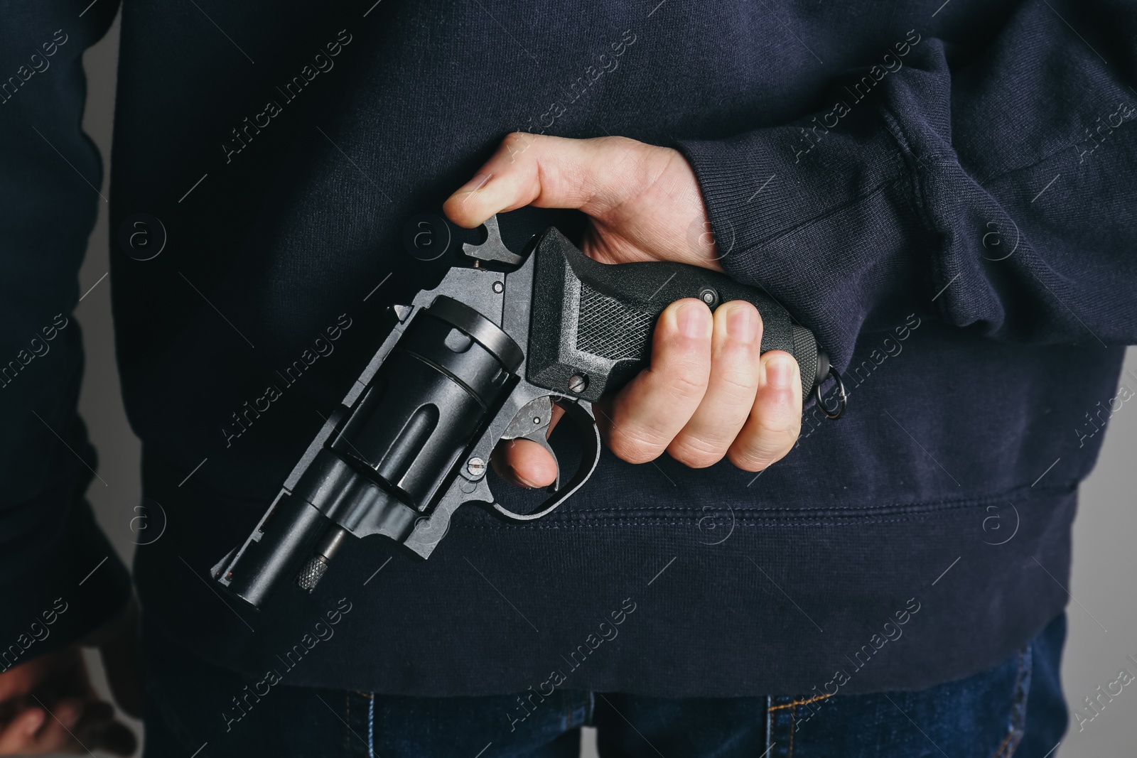 Photo of Man holding gun behind his back on grey background, closeup