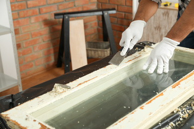 Man repairing old damaged window at table indoors, closeup