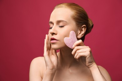 Photo of Beautiful young woman doing facial massage with gua sha tool on pink background