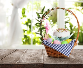Image of Basket with delicious Easter cake and painted eggs on wooden table indoors. Space for text