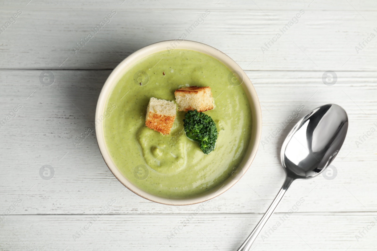 Photo of Delicious broccoli cream soup with croutons served on white wooden table, flat lay