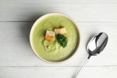 Photo of Delicious broccoli cream soup with croutons served on white wooden table, flat lay