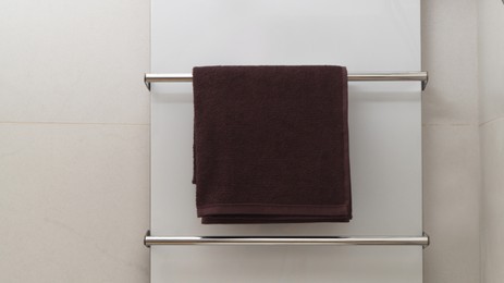 Photo of Brown soft towel on modern heated rail in bathroom, space for text