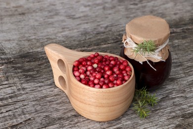 Photo of Tasty lingonberry jam in jar and cup with red berries on wooden table