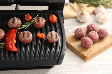 Photo of Electric grill with vegetables, meat balls and rosemary on wooden table