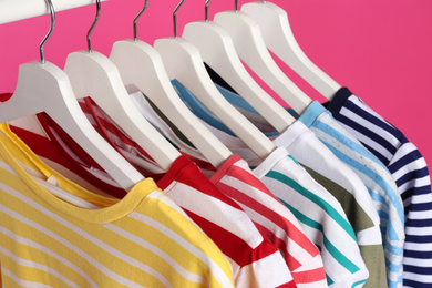 Photo of Colorful clothes on hangers against pink background, closeup