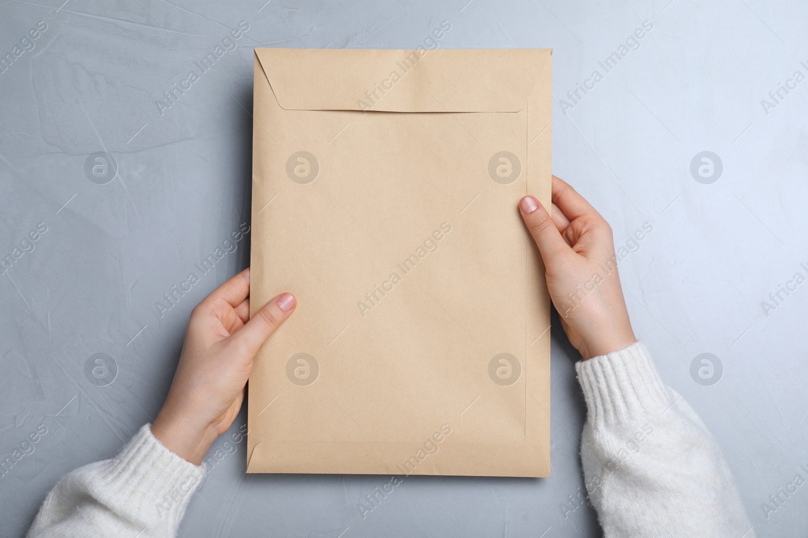 Photo of Woman with kraft paper envelope at grey table, top view