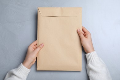 Photo of Woman with kraft paper envelope at grey table, top view