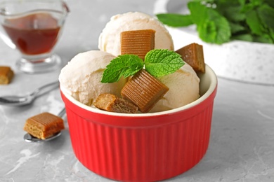 Bowl of delicious ice cream with caramel candies and mint on light grey marble table, closeup