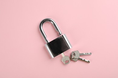 Photo of Modern padlock with keys on pink background, top view