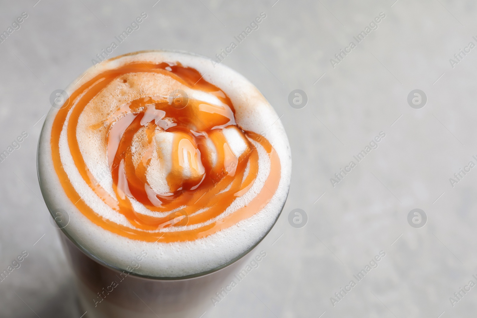 Photo of Glass with delicious caramel latte on light background, closeup