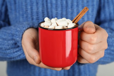 Photo of Woman holding cup of delicious hot chocolate with marshmallows and cinnamon stick, closeup