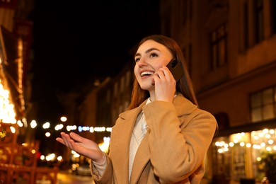 Photo of Beautiful woman talking by smartphone on night city street