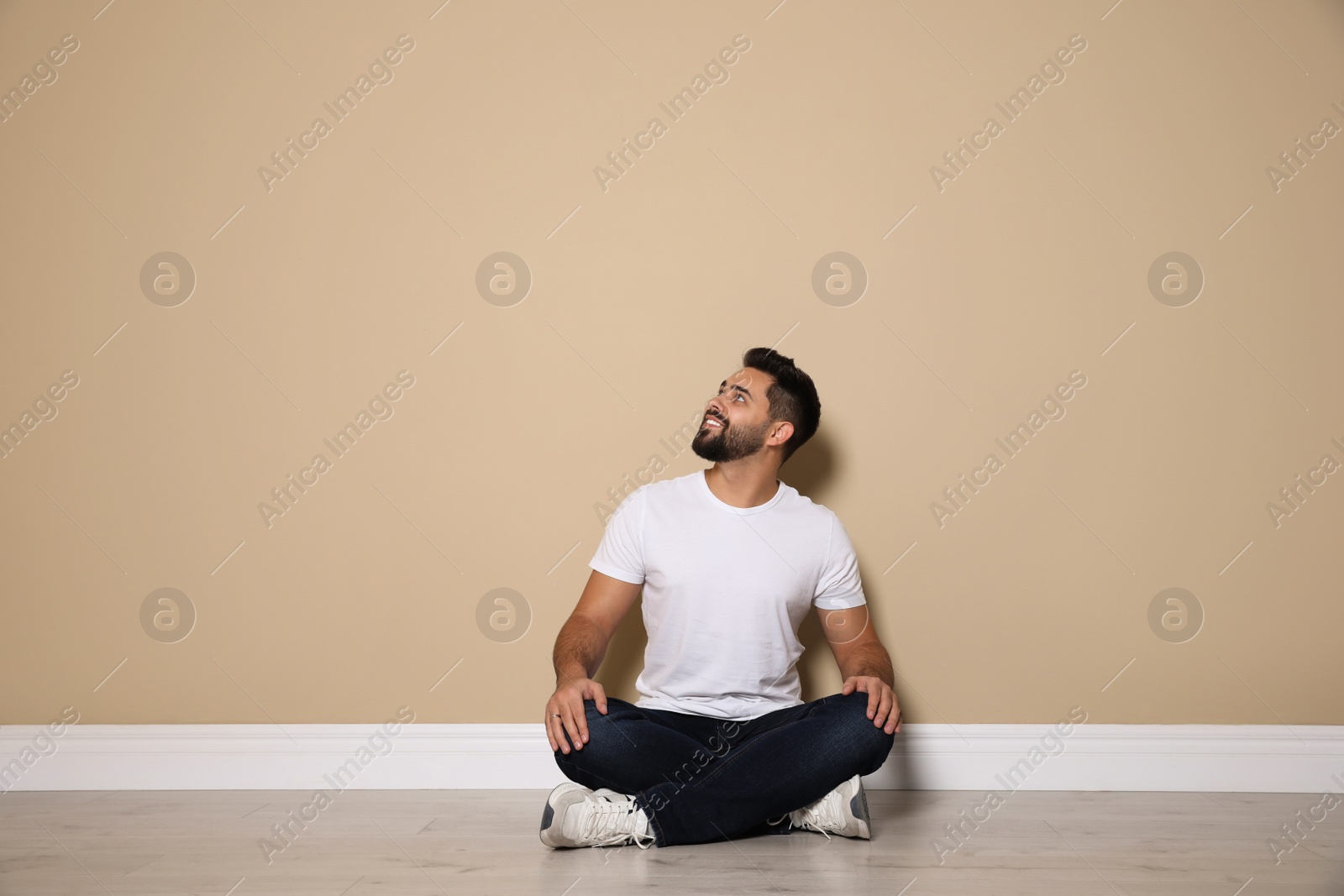 Photo of Young man sitting on floor near beige wall indoors