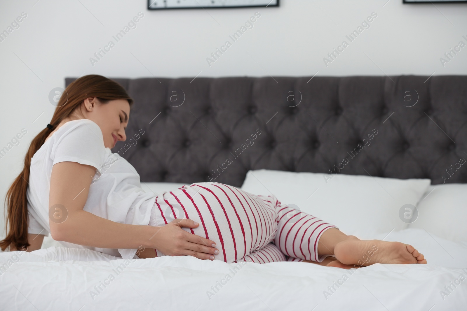 Photo of Young woman suffering from hemorrhoid on bed at home