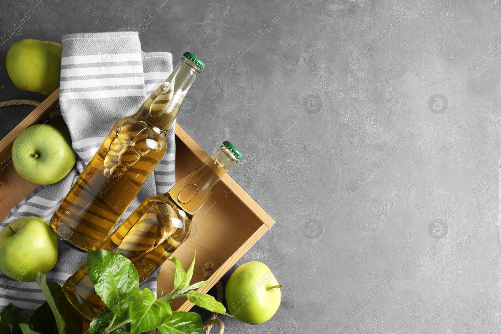 Photo of Delicious cider, ripe apples and green leaves on gray table, flat lay. Space for text