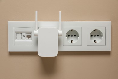 Wireless Wi-Fi repeater in power socket on beige wall