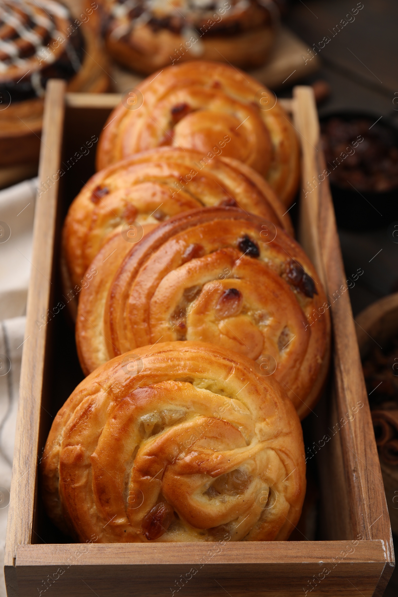 Photo of Delicious rolls with raisins in wooden box on table, closeup. Sweet buns