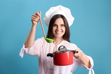Photo of Happy young woman with cooking pot and ladle on light blue background