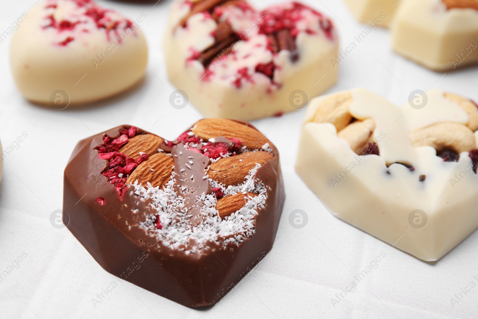 Photo of Tasty chocolate heart shaped candies with nuts on white tiled table, closeup