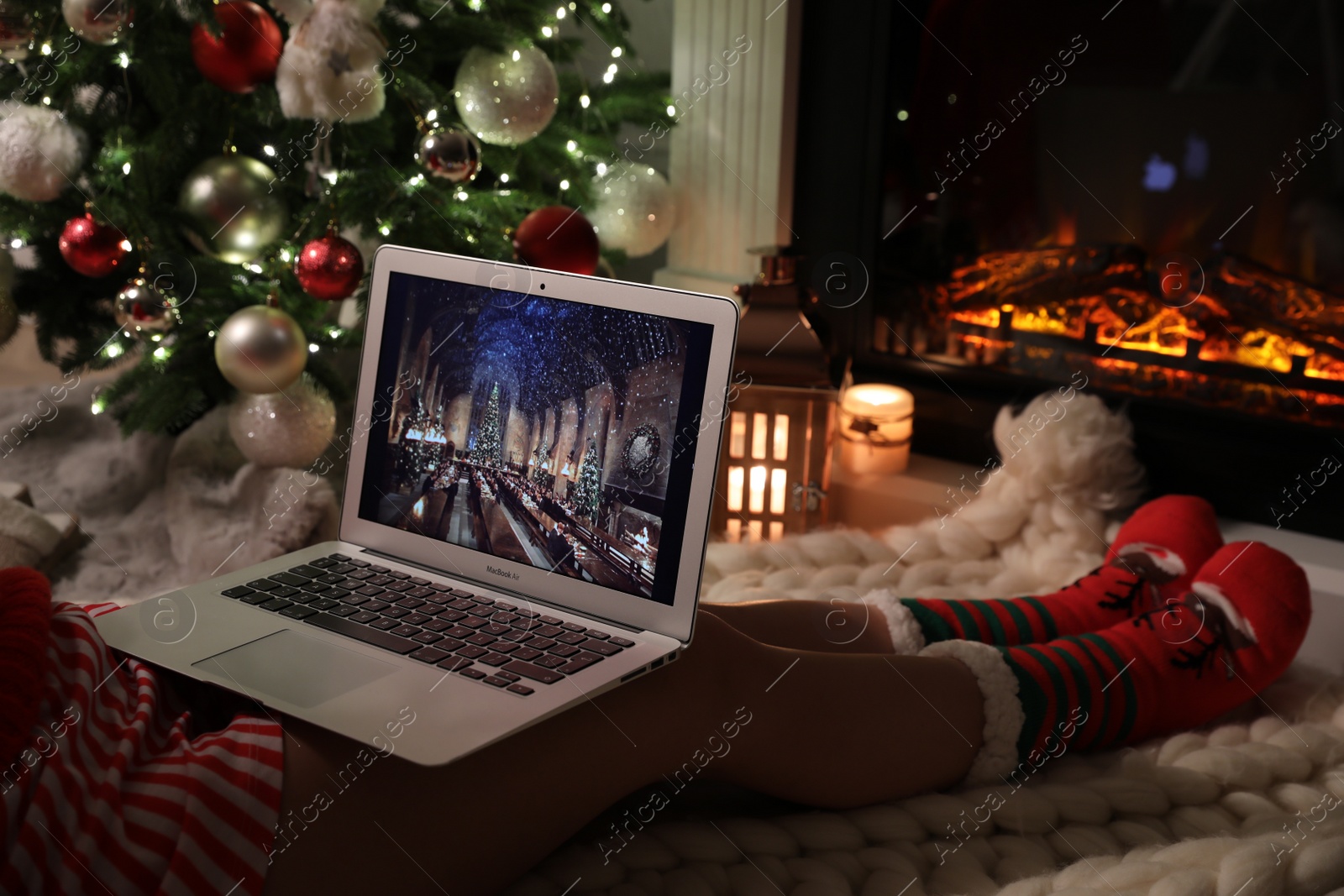 Photo of MYKOLAIV, UKRAINE - DECEMBER 23, 2020: Woman watching Harry Potter and Philosopher's Stone movie on laptop near fireplace at home, closeup. Cozy winter holidays atmosphere