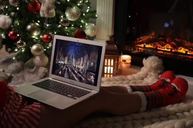 Photo of MYKOLAIV, UKRAINE - DECEMBER 23, 2020: Woman watching Harry Potter and Philosopher's Stone movie on laptop near fireplace at home, closeup. Cozy winter holidays atmosphere