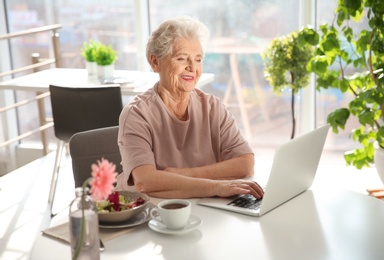 Photo of Elderly woman using laptop while having breakfast at home