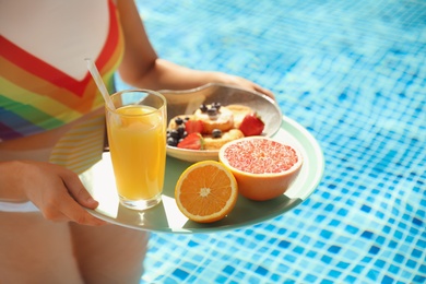 Photo of Young woman with delicious breakfast on tray in swimming pool, closeup