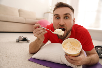 Photo of Lazy young man eating ice cream instead of training at home