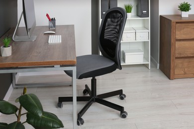 Stylish office chair near desk with computer in room. Interior design