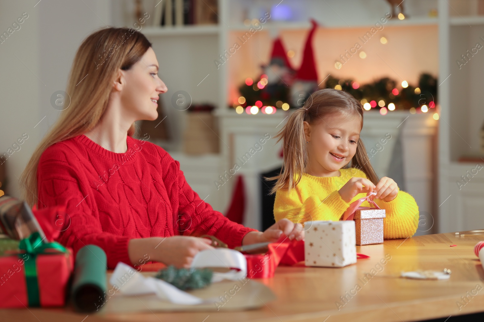 Photo of Christmas presents wrapping. Mother and her little daughter decorating gift box with ribbon at home