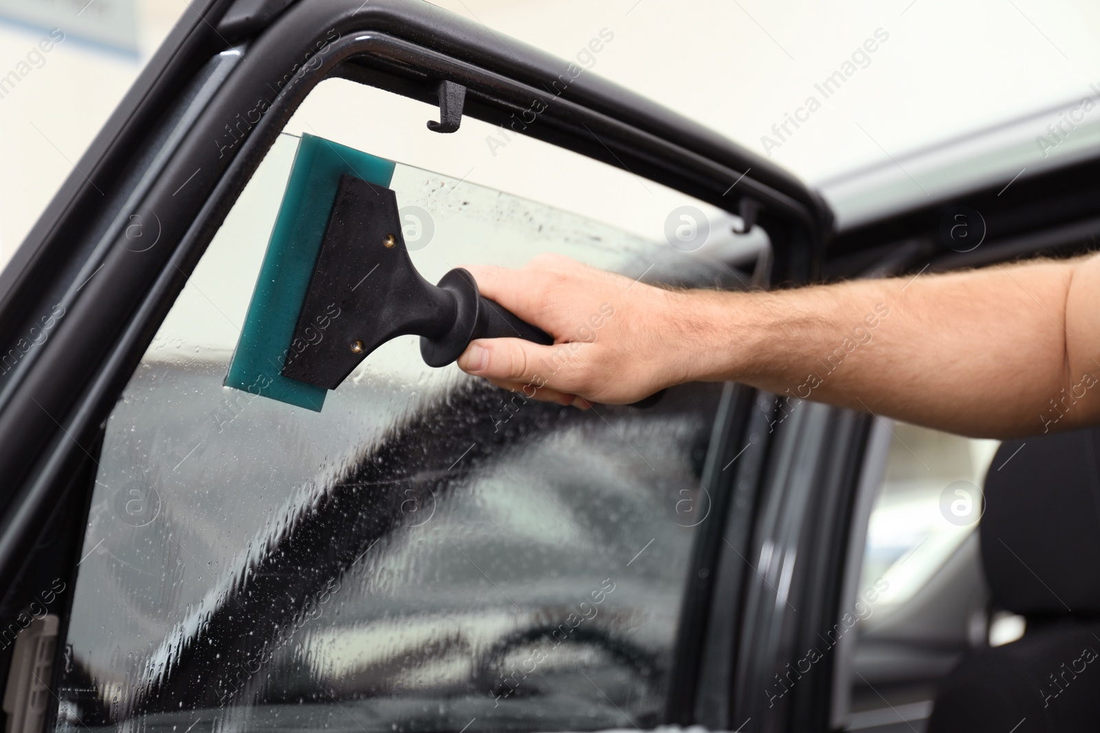 Photo of Worker washing tinted car window in workshop, closeup