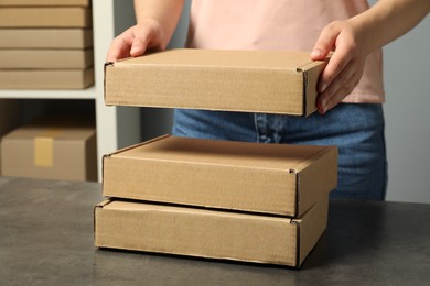 Photo of Packaging goods. Woman with cardboard boxes at grey table indoors, closeup