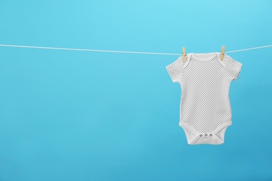 Baby onesie hanging on clothes line against blue background, space for text. Laundry day