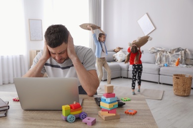 Photo of Children disturbing stressed man in living room. Working from home during quarantine