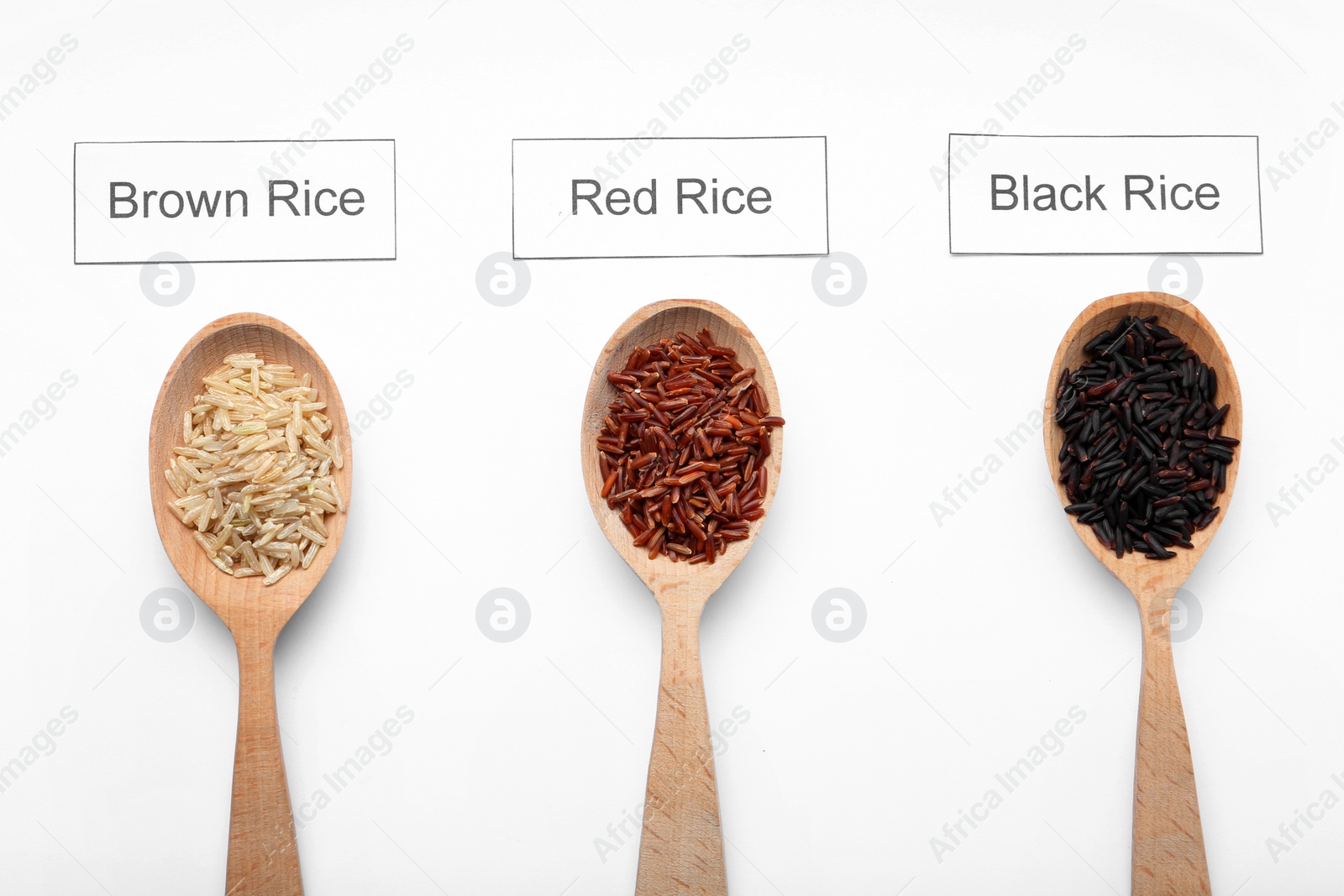 Photo of Spoons with different types of uncooked rice and cards on white background, top view