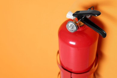 Photo of Red fire extinguisher on orange wall, closeup. Space for text