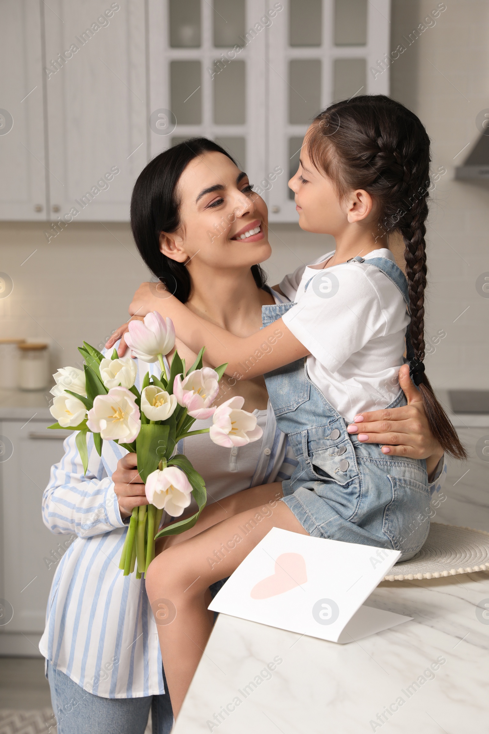 Photo of Little daughter congratulating her mom in kitchen at home. Happy Mother's Day