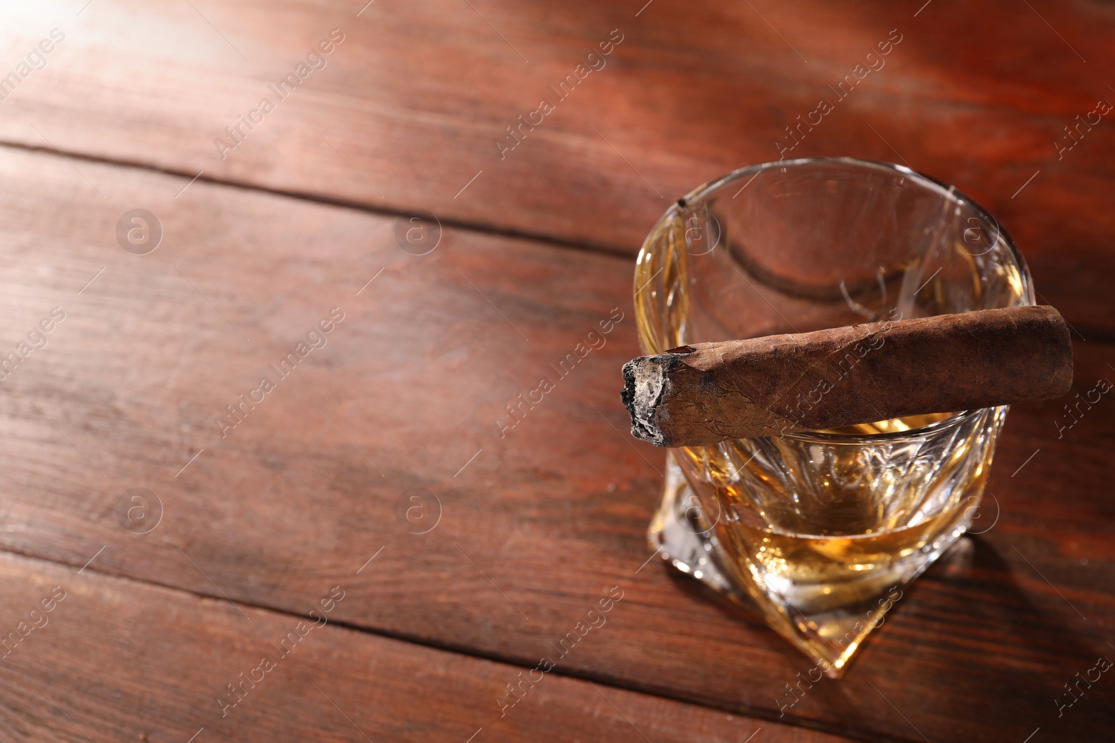 Photo of Glass of whiskey and burnt cigar on wooden table, above view. Space for text