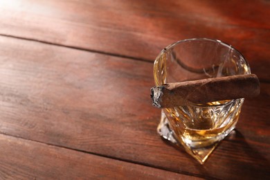 Photo of Glass of whiskey and burnt cigar on wooden table, above view. Space for text